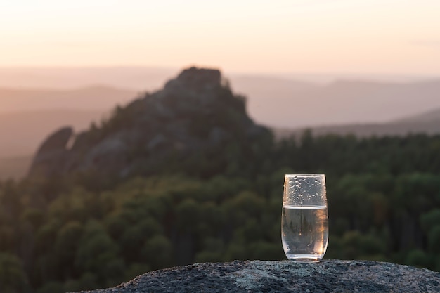 Un vaso de agua mineral pura en un vaso transparente contra el en las montañas