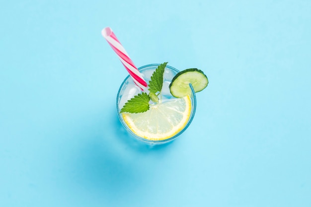 Un vaso de agua o bebida con hielo, limón, pepino y menta sobre una superficie azul. El concepto de verano caluroso, alcohol, bebidas refrescantes, calmar la sed, bar. Vista plana, vista superior