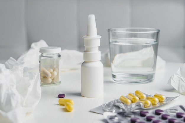 Vaso de agua, pastillas de aerosol nasal en blister y pañuelos de papel usados en la mesa Concepto de tratamiento de la gripe