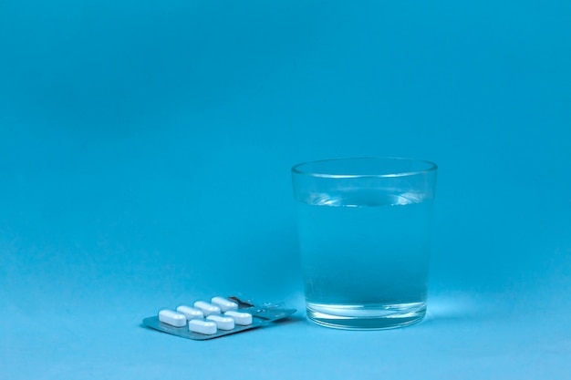 Vaso de agua y pastillas sobre fondo azul.