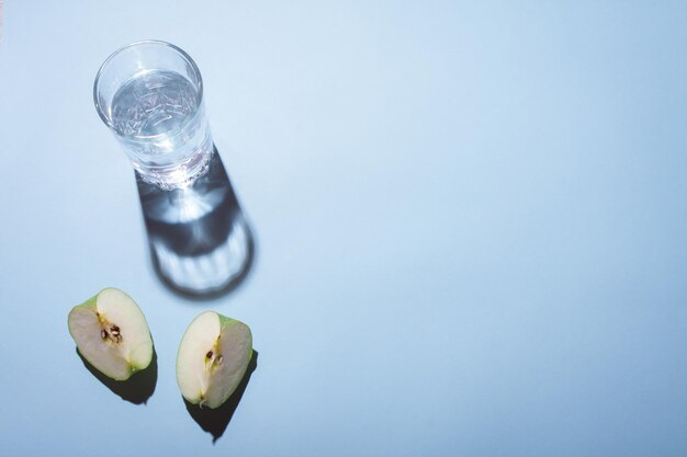 Un vaso de agua y pedazos de manzana sobre un fondo azul.