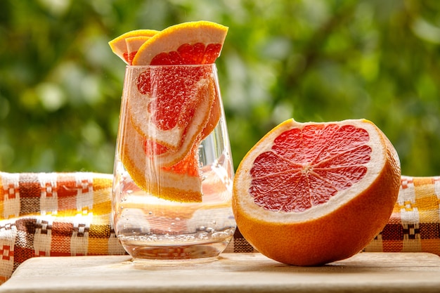 Un vaso de agua con pomelo en el fondo del jardín.