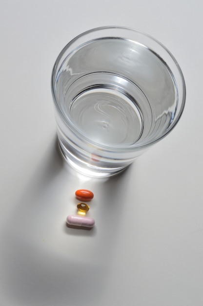 Un vaso de agua potable y varias cápsulas con vitaminas. fondo claro. de cerca.