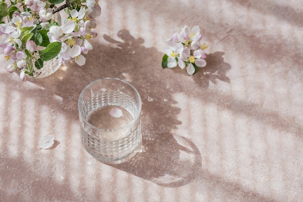 Vaso de agua pura sobre la mesa con rama de manzano en flor en un vaso