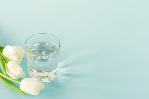 Un vaso de agua pura con tulipanes sobre fondo azul. Copie el espacio para el texto. concepto de salud, vida y dieta.