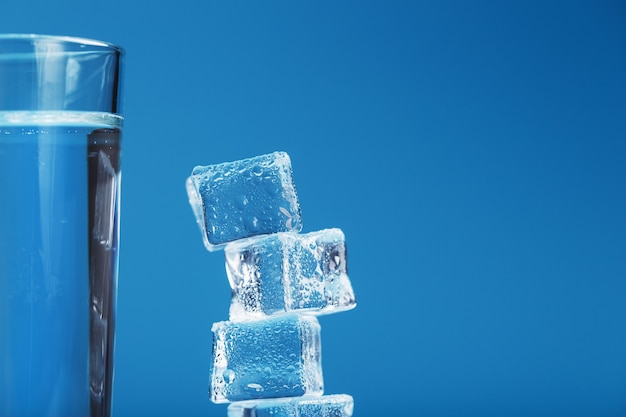 Un vaso de agua refrescante y una torre de cubitos de hielo sobre un fondo azul.