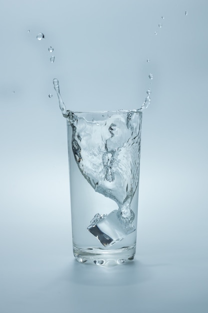 Vaso de agua con salpicaduras de cubitos de hielo cayendo