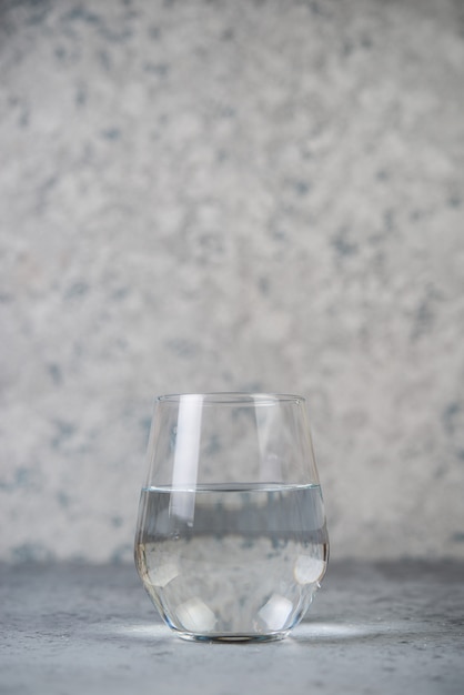 Un vaso de agua sobre una superficie de hormigón gris. Foto vertical.