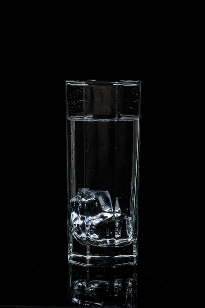 Vaso de agua transparente con cubitos de hielo sobre fondo negro de vidrio aislado