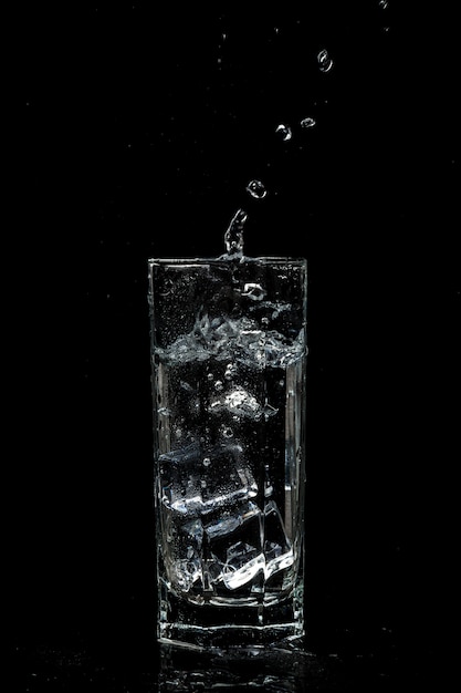 Vaso de agua transparente con cubitos de hielo sobre fondo negro de vidrio aislado