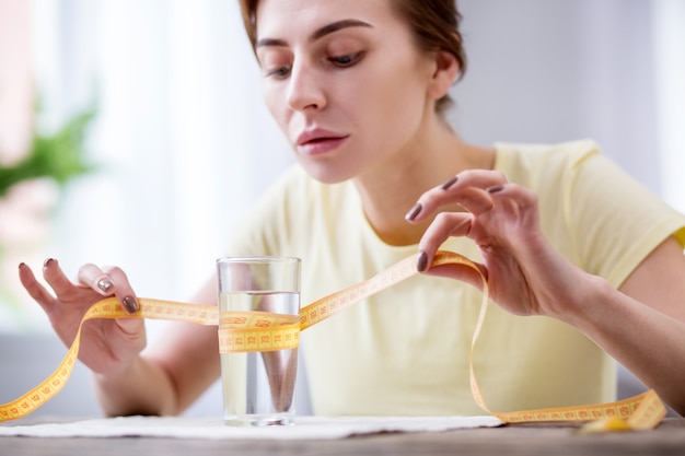 Vaso de agua. Triste mujer deprimida sentada en la mesa mientras mira el vaso de agua