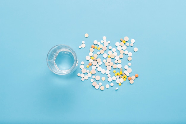 Vaso de agua y varias píldoras sobre un fondo azul. El concepto de tomar drogas en caso de enfermedad y enfermedad. Vista plana, vista superior