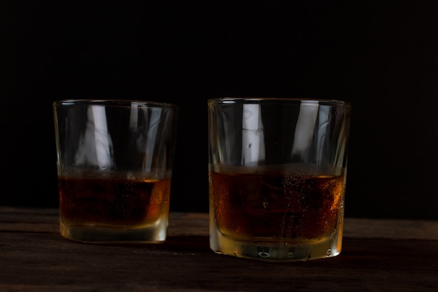 Vaso de alcohol whisky escocés con hielo en mesa de madera