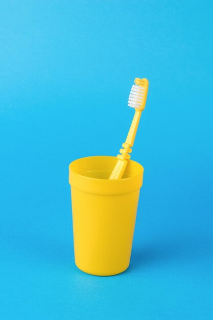 Un vaso amarillo con un cepillo de dientes amarillo sobre un fondo azul claro