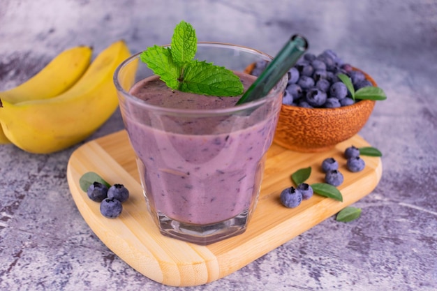 Un vaso de batido de arándanos con un plátano en una tabla de madera