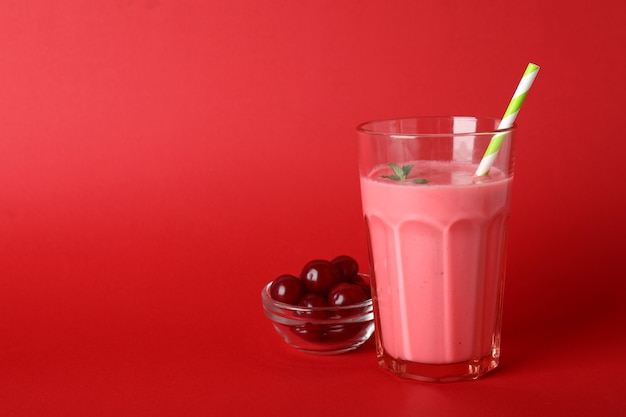 Vaso de batido de cerezas e ingredientes sobre fondo rojo.