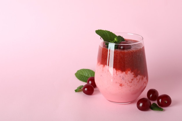 Vaso de batido de cerezas e ingredientes sobre fondo rosa