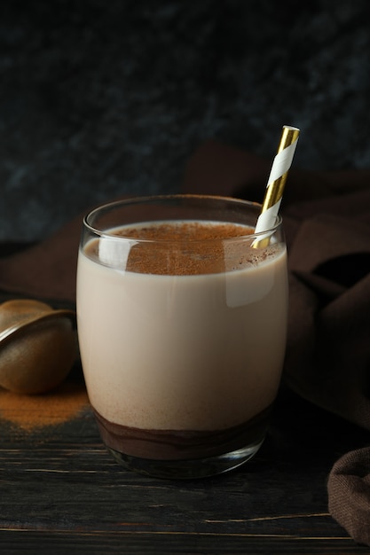 Vaso de batido de chocolate, paño de cocina y tamiz sobre mesa de madera