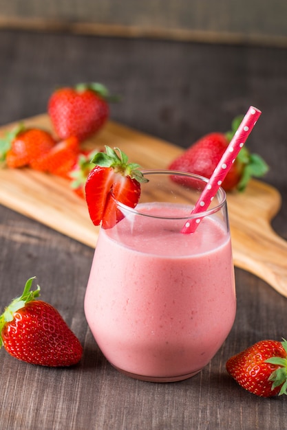 Foto vaso de batido de fresa fresca, batido y fresas frescas sobre fondo rosa, blanco y madera. concepto de comida y bebida saludable.