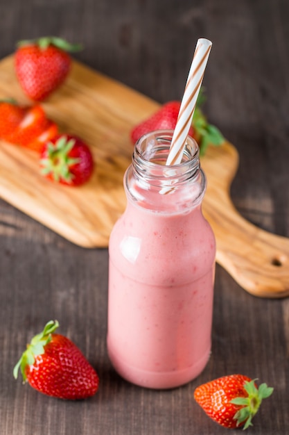 Vaso de batido de fresa fresca, batido y fresas frescas sobre fondo rosa, blanco y madera. Concepto de comida y bebida saludable.