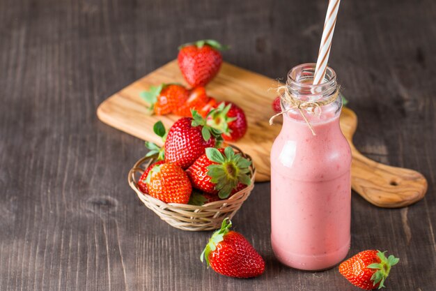 Vaso de batido de fresa fresca, batido y fresas frescas sobre fondo rosa, blanco y madera. Concepto de comida y bebida saludable.