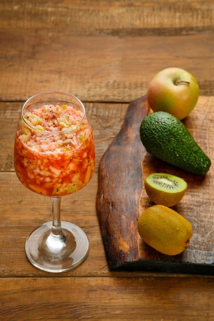 Foto vaso de batido de manzana kiwi fresco sobre una mesa de madera junto a un aguacate de manzana kiwi de tablero negro.