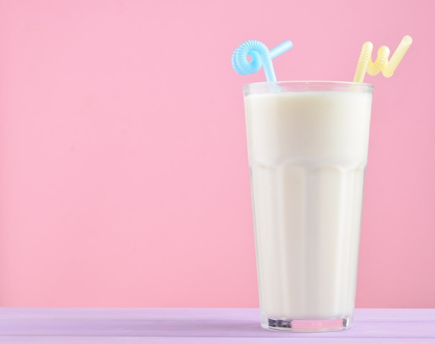 Un vaso de batido con una pajita sobre una mesa de madera de color pastel