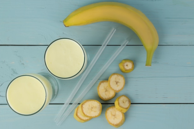 Un vaso con un batido de plátano y un plátano fresco sobre una mesa de madera azul. Hacer un batido. vista superior