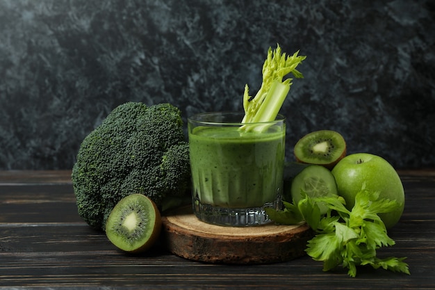 Vaso de batido verde e ingredientes sobre mesa de madera