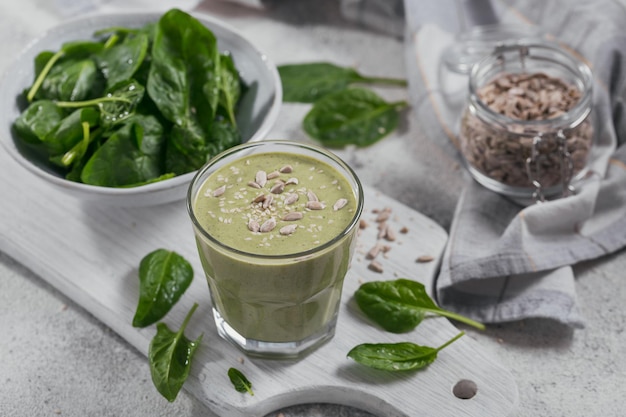 Vaso de batido verde saludable casero con espinacas frescas, girasoles y semillas de sésamo sobre fondo claro. Concepto de comida y bebida, dieta y alimentación saludable.