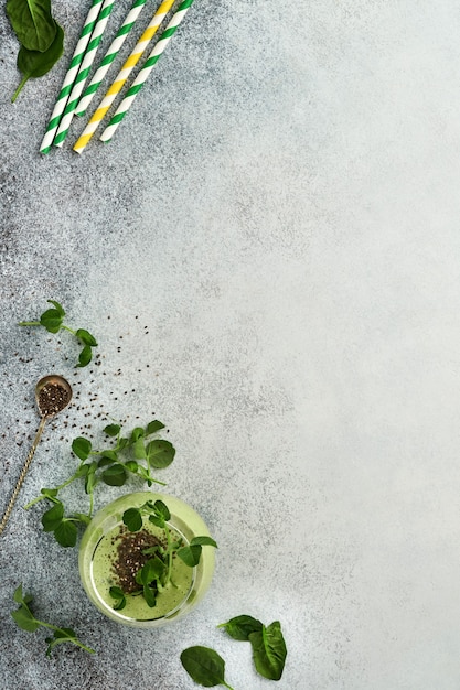 Vaso de batido verde saludable e ingredientes para batido, espinacas frescas, microvegetales de guisantes, plátano, kiwi, manzana y semillas de chía sobre fondo de hormigón gris claro. Bebidas saludables para comer. Vista superior.