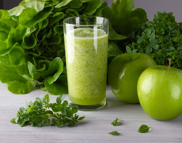 Un vaso de batido verde saludable con manzana y hojas sobre la mesa de madera blanca