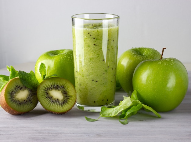 Un vaso de batido verde saludable con manzana, kiwi y hojas sobre la mesa de madera blanca