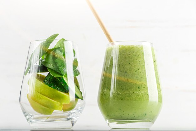 Vaso con batido verde y vaso con ingredientes espinaca, manzana, pepino. Cocina casera. Comida vegana de desintoxicación saludable, bebida dietética y para bajar de peso.