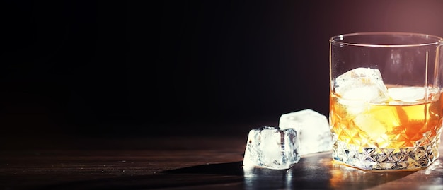 Un vaso de bebida alcohólica fuerte con hielo en una barra de bar de madera. Whisky con cubitos de hielo. Vaso con bebida fría.