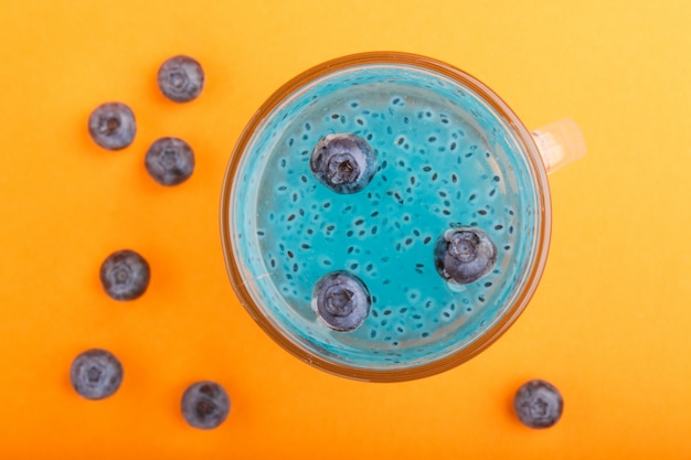 Vaso de bebida de color azul arándano con semillas de albahaca sobre fondo naranja Concepto de bebida saludable de primavera Morninig