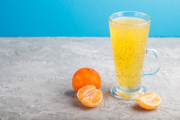 Vaso de bebida de color naranja mandarina con semillas de albahaca sobre una superficie gris. Vista lateral
