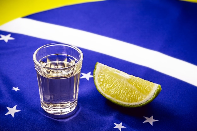 Vaso de bebida destilada a base de caña de azúcar, sobre la bandera brasileña, concepto del día nacional de "goteo" y cachaça