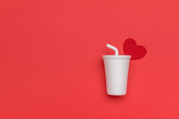 Foto un vaso blanco con un tubo y un corazón rojo sobre un fondo rojo.