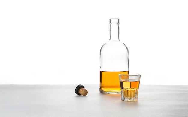 Un vaso y una botella de alcohol con un corcho sobre un fondo blanco.