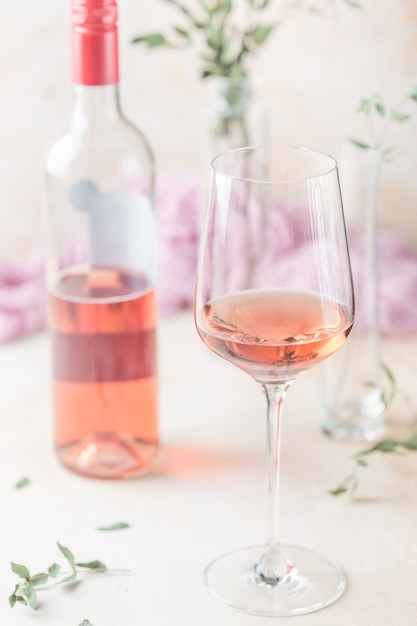 Vaso y botella de vino rosado sobre fondo claro.