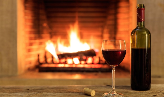 Foto un vaso y una botella de vino tinto en el fondo de la chimenea en llamas