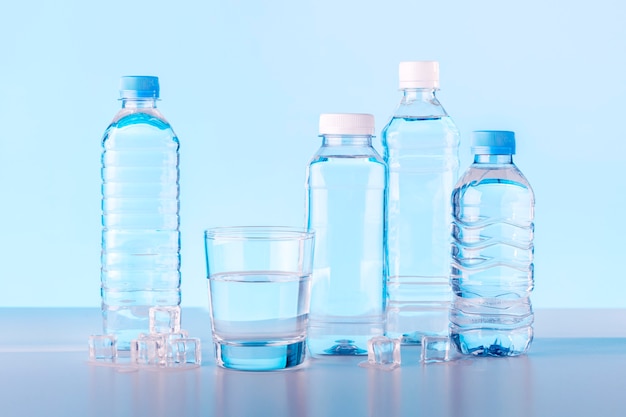 Vaso y botellas de agua sobre fondo azul.