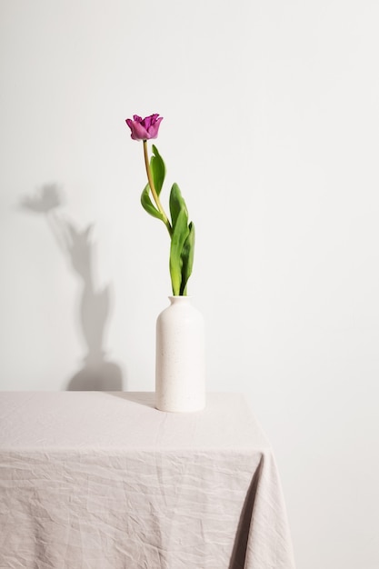 Vaso branco com tulipa rosa na mesa com toalha bege