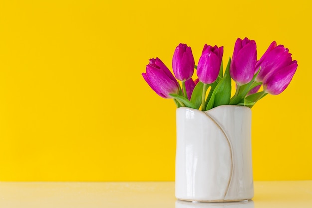 Vaso branco com tulipas roxas em um fundo amarelo