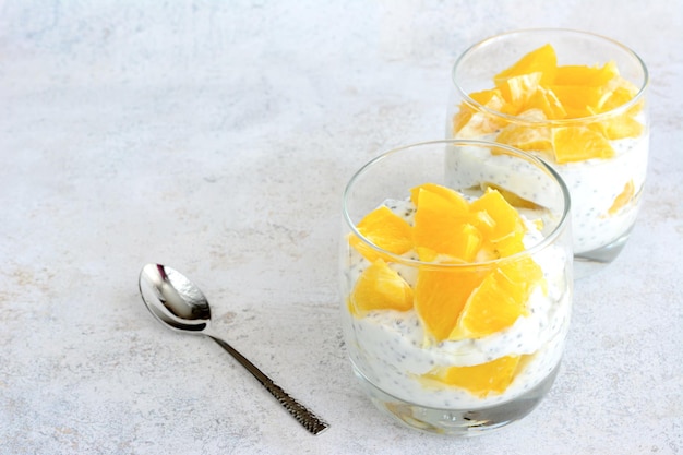 Un vaso de budín de chía de mango con una cuchara sobre una mesa blanca