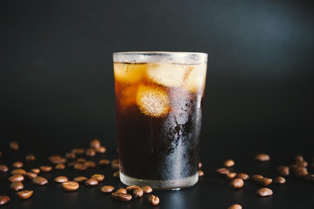 vaso de café americano helado sobre fondo negro con granos de café