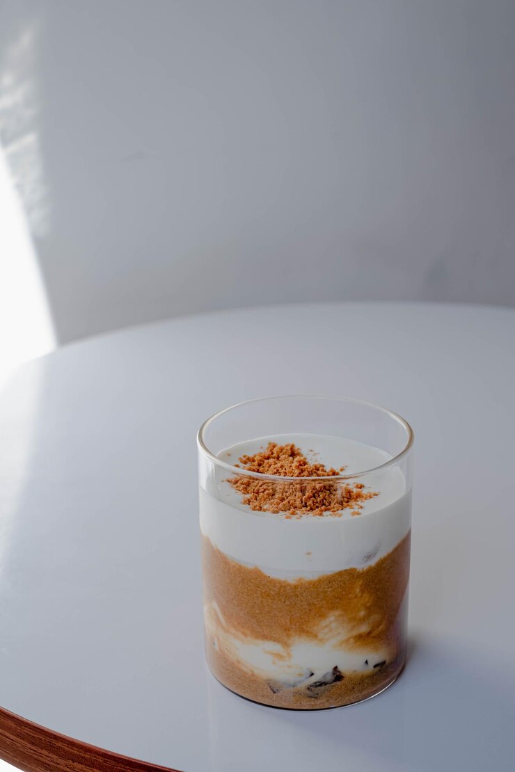 Un vaso de café con crema de leche batida y oblea triturada que se espolvorea sobre la superficie en una mesa blanca