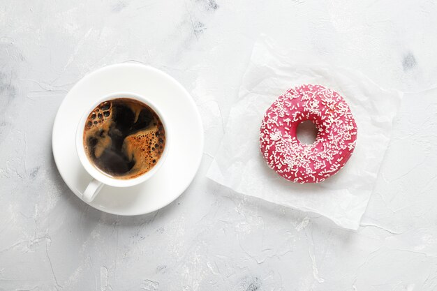 Vaso con café y donut dulce sabroso sobre un fondo claro con lugar para el texto.