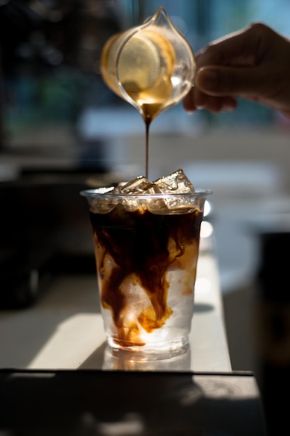 Un vaso de café helado con hielo y una botella de café que se vierte en él.